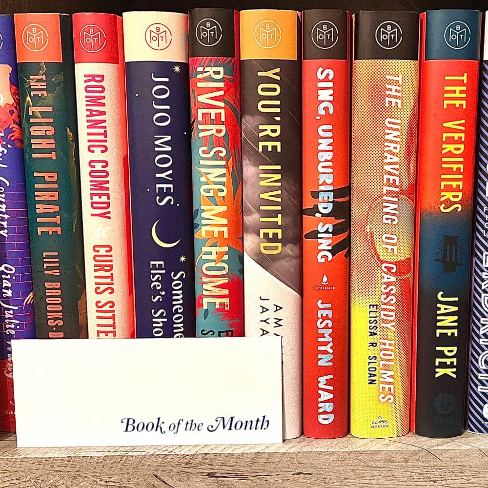 Row of hardcover Book of the Month club books, with a Book of the Month bookmark sitting in front of them.