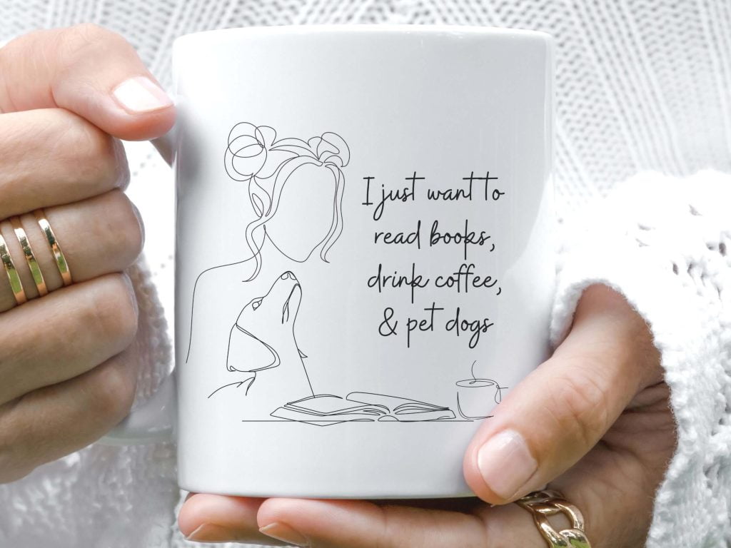 White mug with a line drawing of a woman reading a book beside a dog, reading I just want to read books, drink coffee, and pet dogs