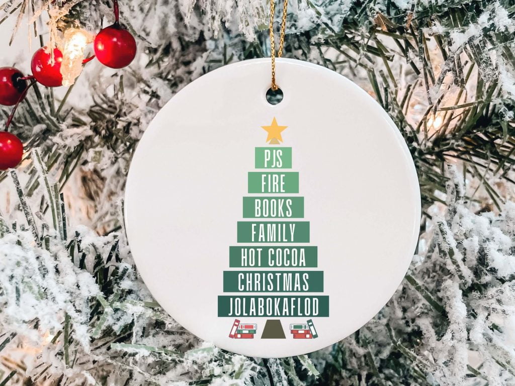 White ornament with a layered Christmas tree, reading from the top down: PJs, Fire, Books, Family, Hot Cocoa, Christmas, Jolabokaflod