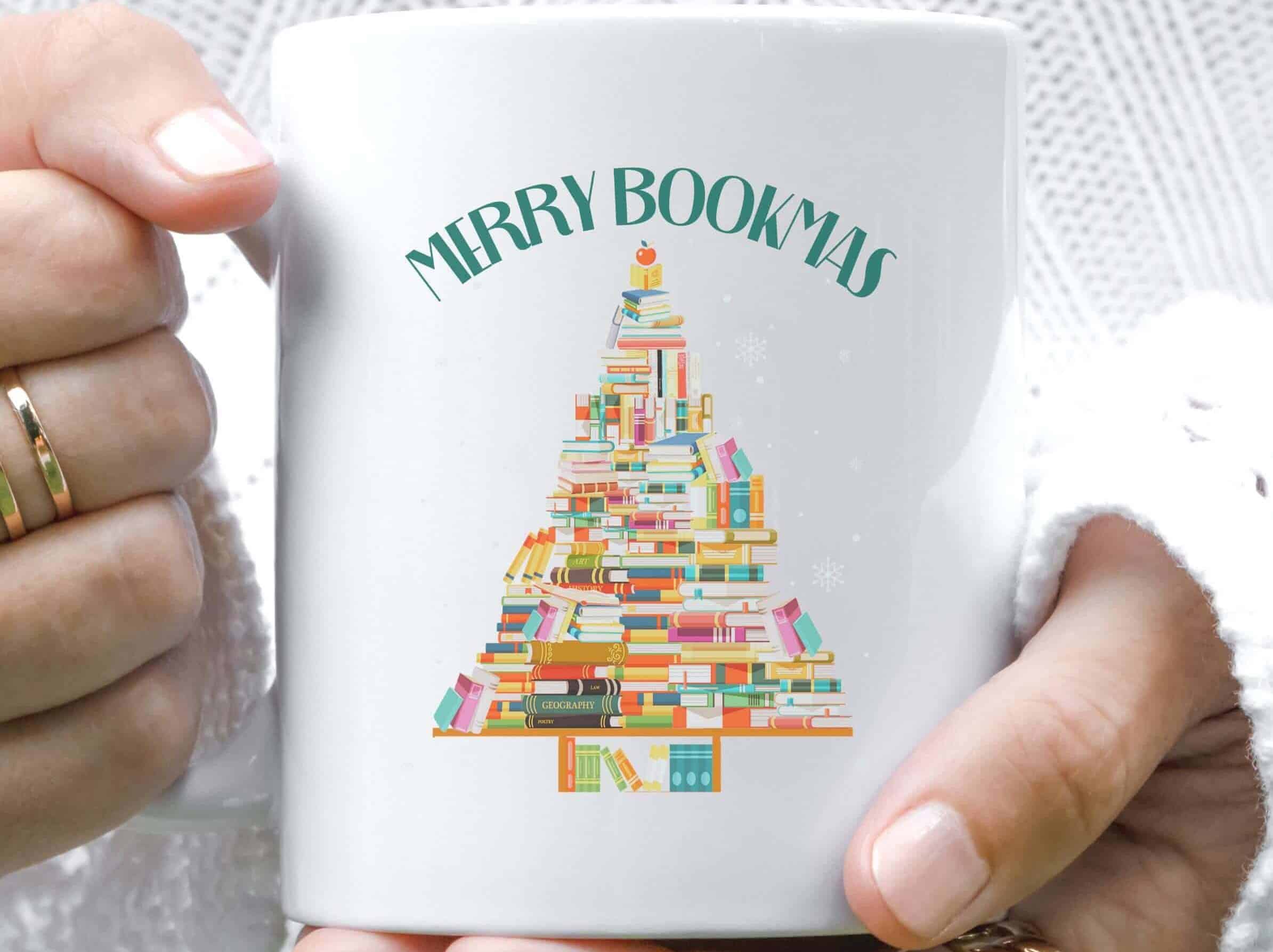 Hands holding a mug that reads Merry Bookmas and has a Christmas tree made of a stack of books