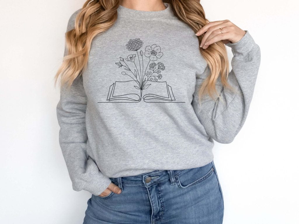 Woman wearing a sweatshirt with a line drawing of a book with wildflowers growing out of it