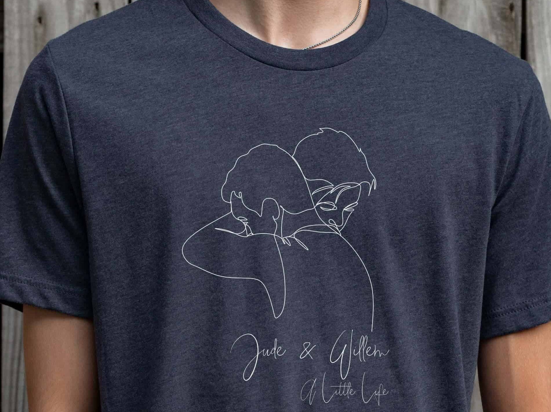 Man wearing a navy tshirt with a line drawing of two men hugging, with a label reading Jude and Willem, A Little Life
