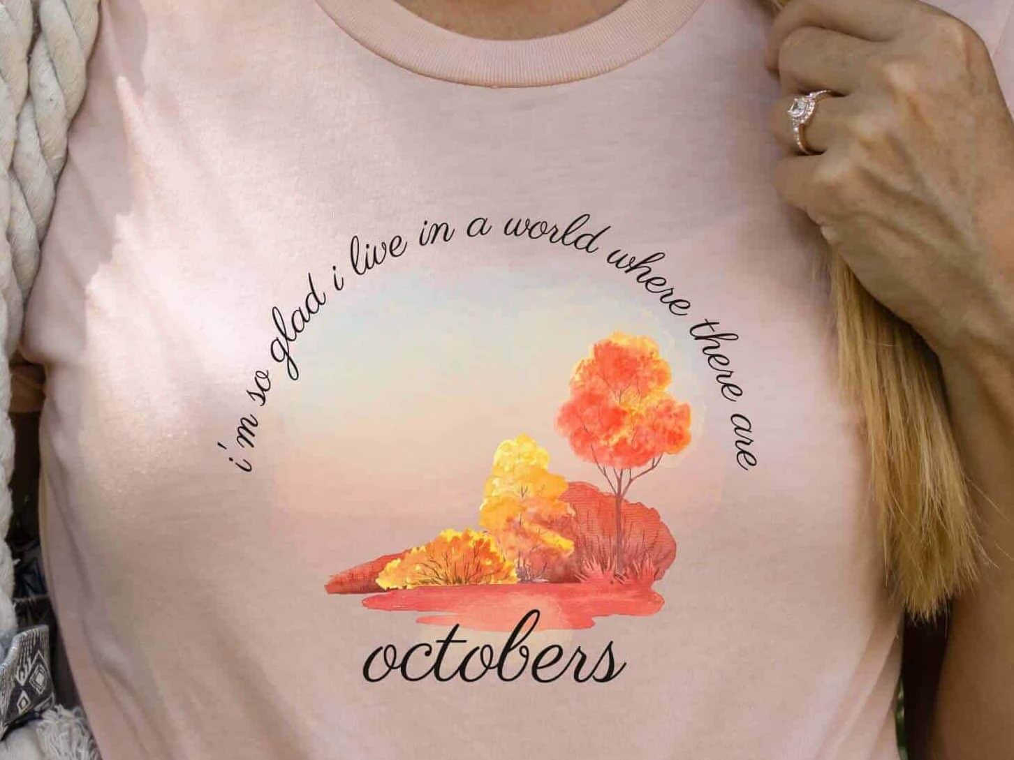 Woman wearing a peach colored shirt with the quote, I'm so glad I live in a world where there are Octobers from Anne of Green Gables.